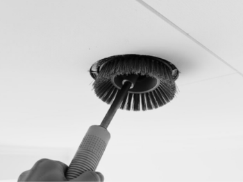 Børste som rengjør en rund avtrekksventil i taket under ventilasjonsrens i en bolig.